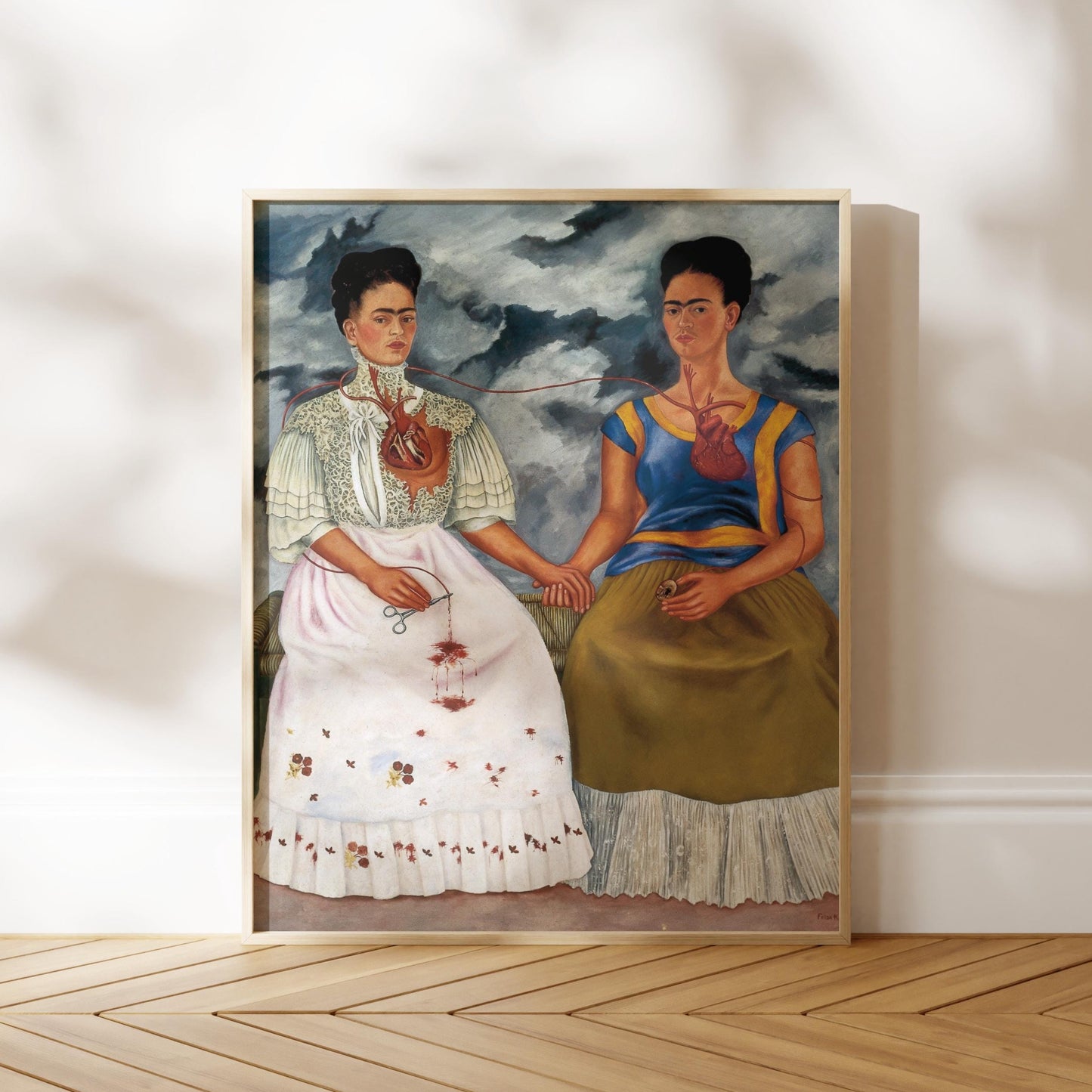 The image is a framed painting depicting two women in traditional Mexican dresses, with one woman wearing a white dress and the other wearing a yellow dress.
