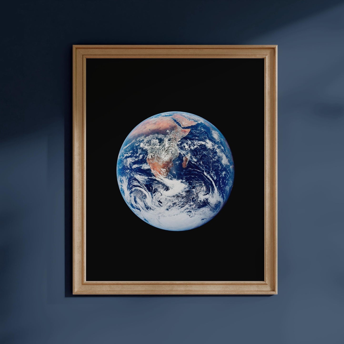 a framed photograph of the Earth, with a dark blue background and a wooden frame.