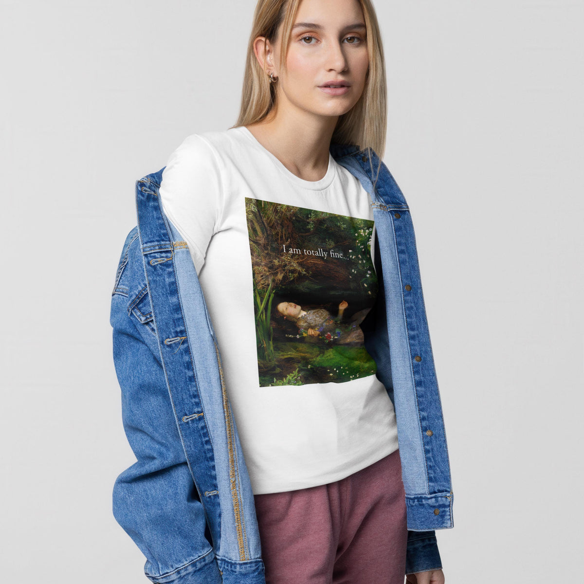 A young woman wearing a white t-shirt with a graphic design, a denim jacket, and pink pants stands against a plain background.