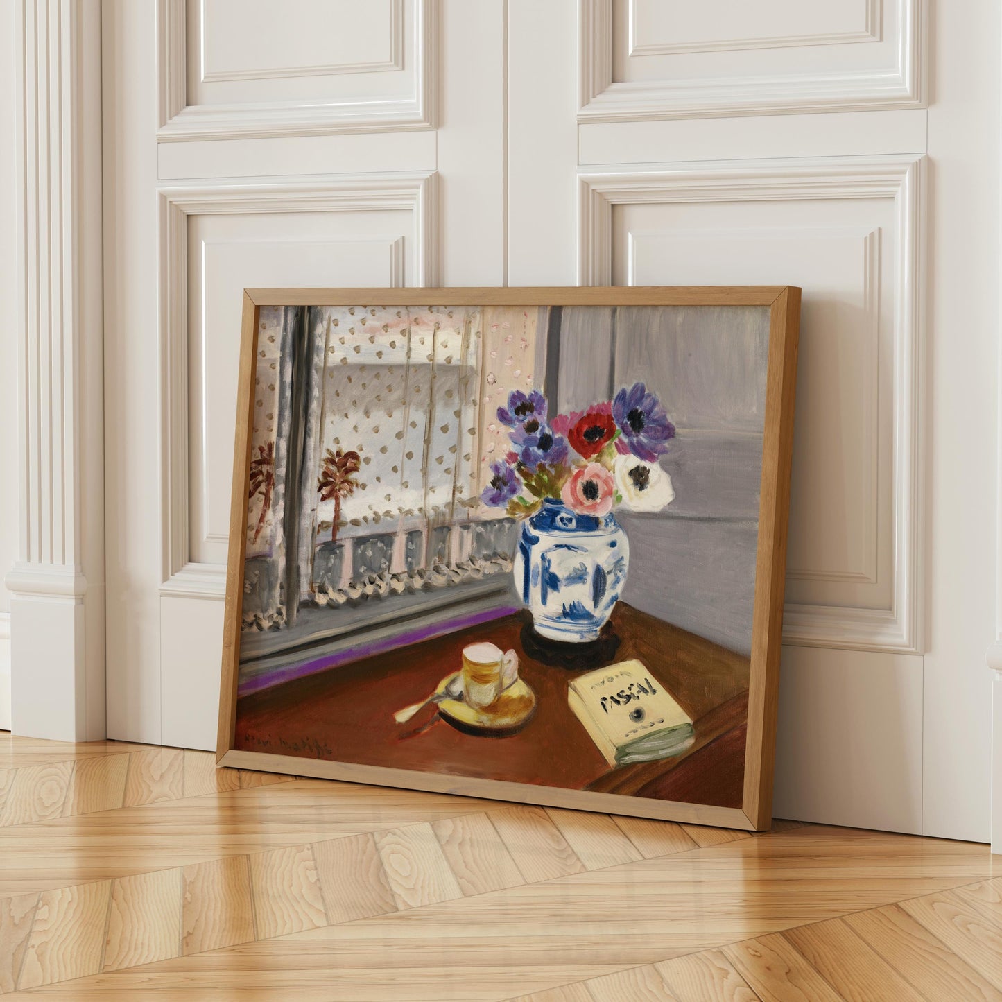 A framed painting depicting a vase of flowers on a table, with a book and a cup of coffee nearby, set against a window with a white curtain.