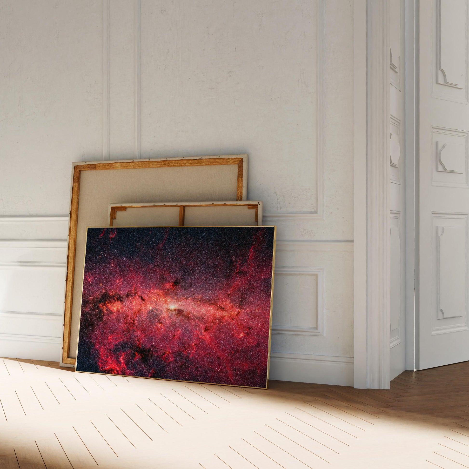 a large, vibrant painting of a galaxy, with a dark background and a bright, colorful foreground. The painting is leaning against a white wall, and there are other paintings stacked on top of it.