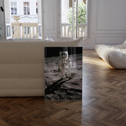 a framed photograph of an astronaut walking on the surface of the moon, with a window and a white couch visible in the background.