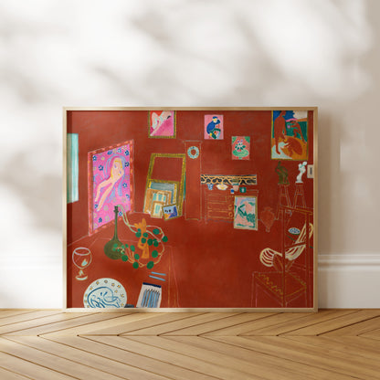 The image is a framed painting depicting a room with various objects, including a vase, a chair, and a table. The painting has a vibrant color palette and is displayed on a wooden floor against a white wall.