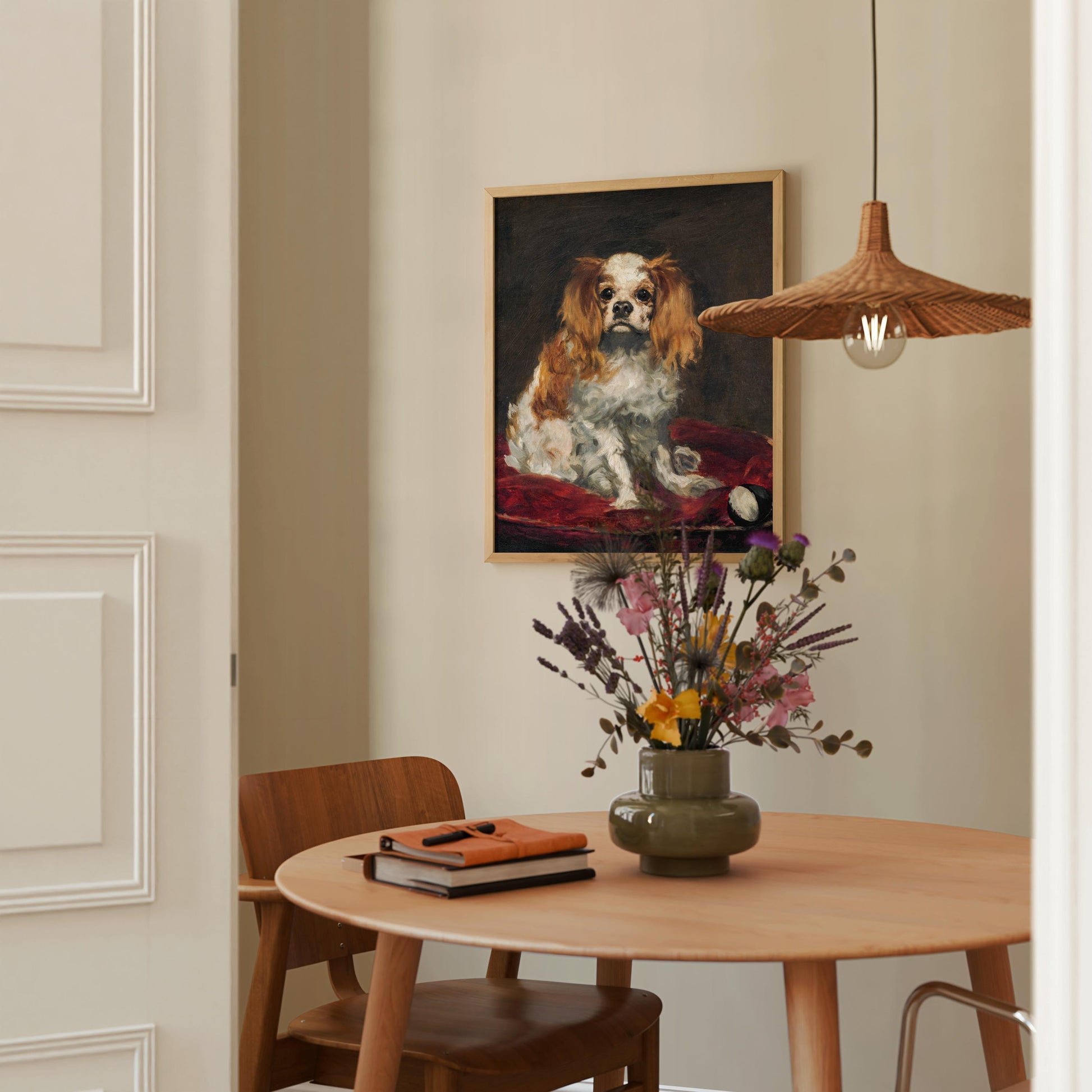 a dining area with a wooden table, a vase of flowers, a book, and a framed painting of a dog.